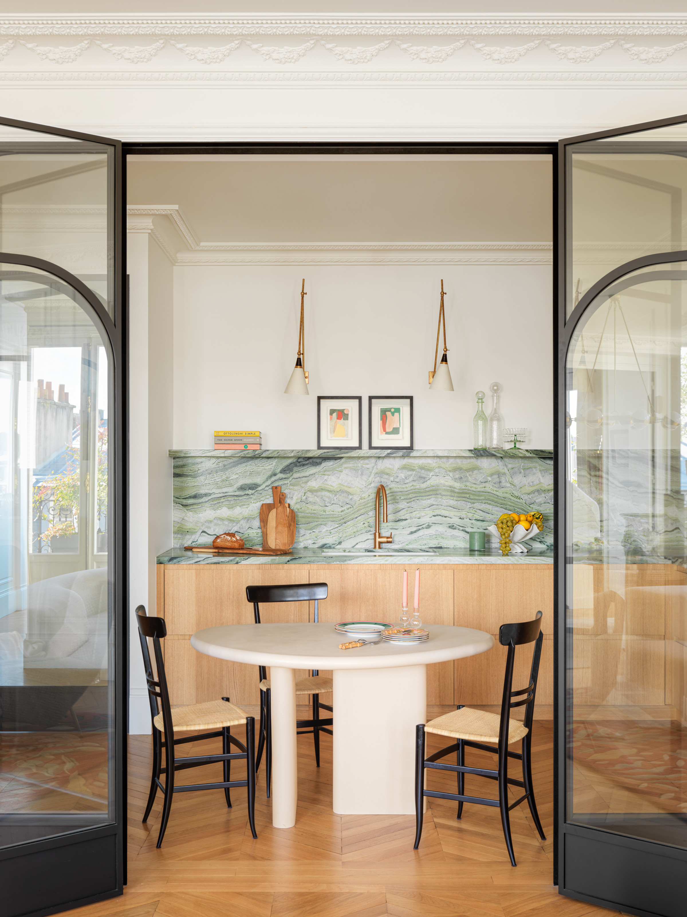 Kitchen with oak cabinetry, green backsplash and counter, and white round breakfast table with black and rattan chairs