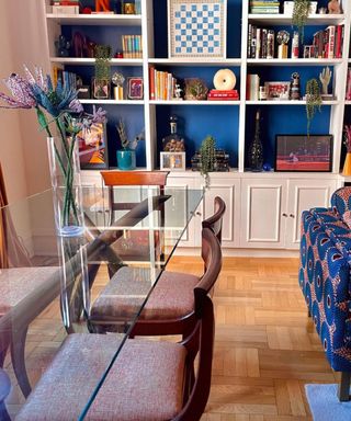 A dining area with a glass table, brown chairs, and a white bookcase with deep blue accents