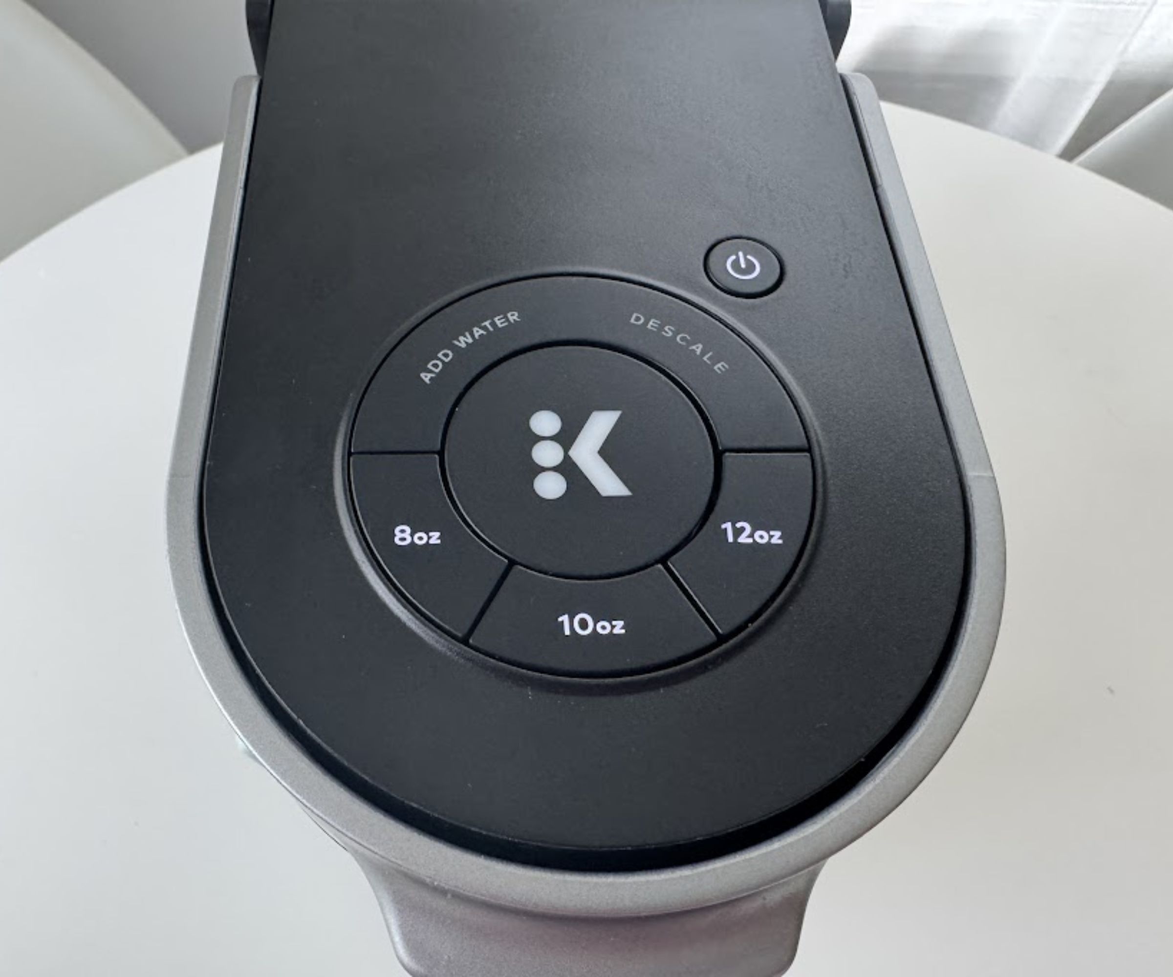 The top of a black Keurig coffee maker, with buttons for an 8oz, 10oz, and 12oz drink, and two warning lights for adding water, and descaling. Next to a round power button.