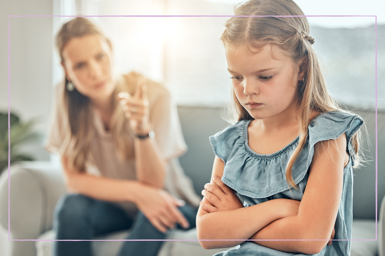 Closeup of an adorable little girl standing with arms crossed and looking upset while being scolded and reprimanded by her angry and disappointed mother at home