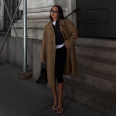 Woman wears trench coat, knit jumper, white long sleeve top, capris and sandals