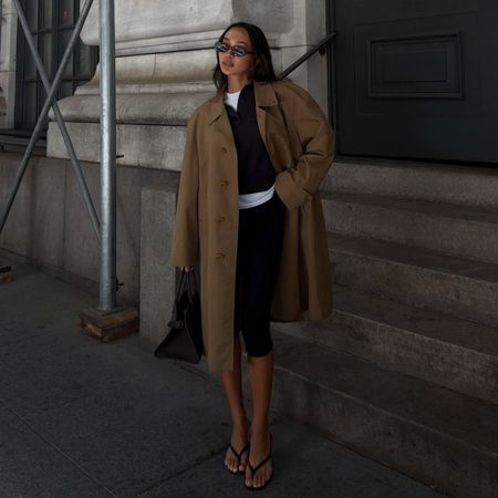 Woman wears trench coat, knit jumper, white long sleeve top, capris and sandals