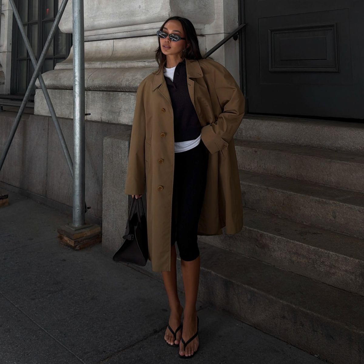 Woman wears trench coat, knit jumper, white long sleeve top, capris and sandals