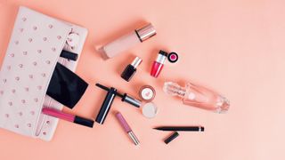 A spilled open bag of makeup with foundation, mascara, perfume and lip gloss