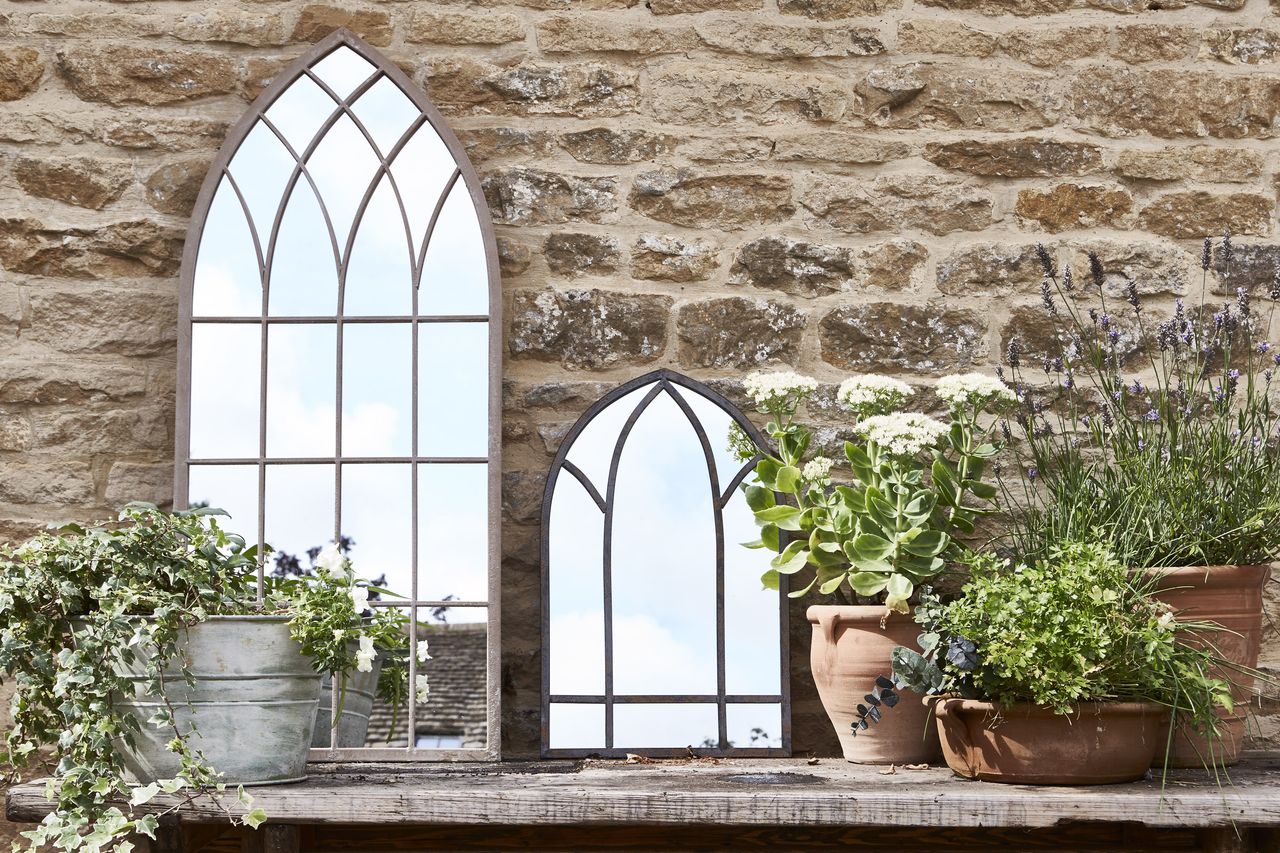 two gothic-style mirrors on a table propped against a stone wall