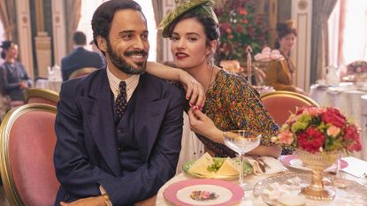 the pursuit of love: Assaad Bouab as Fabrice de Sauveterre and Lily James as Linda Radlett sitting at a table with champagne saucers