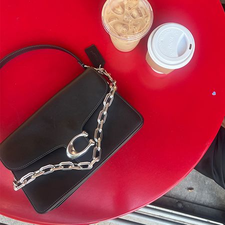pictured is a black coach chain tabby with silver hardware laying on a red table with two beverages next to it