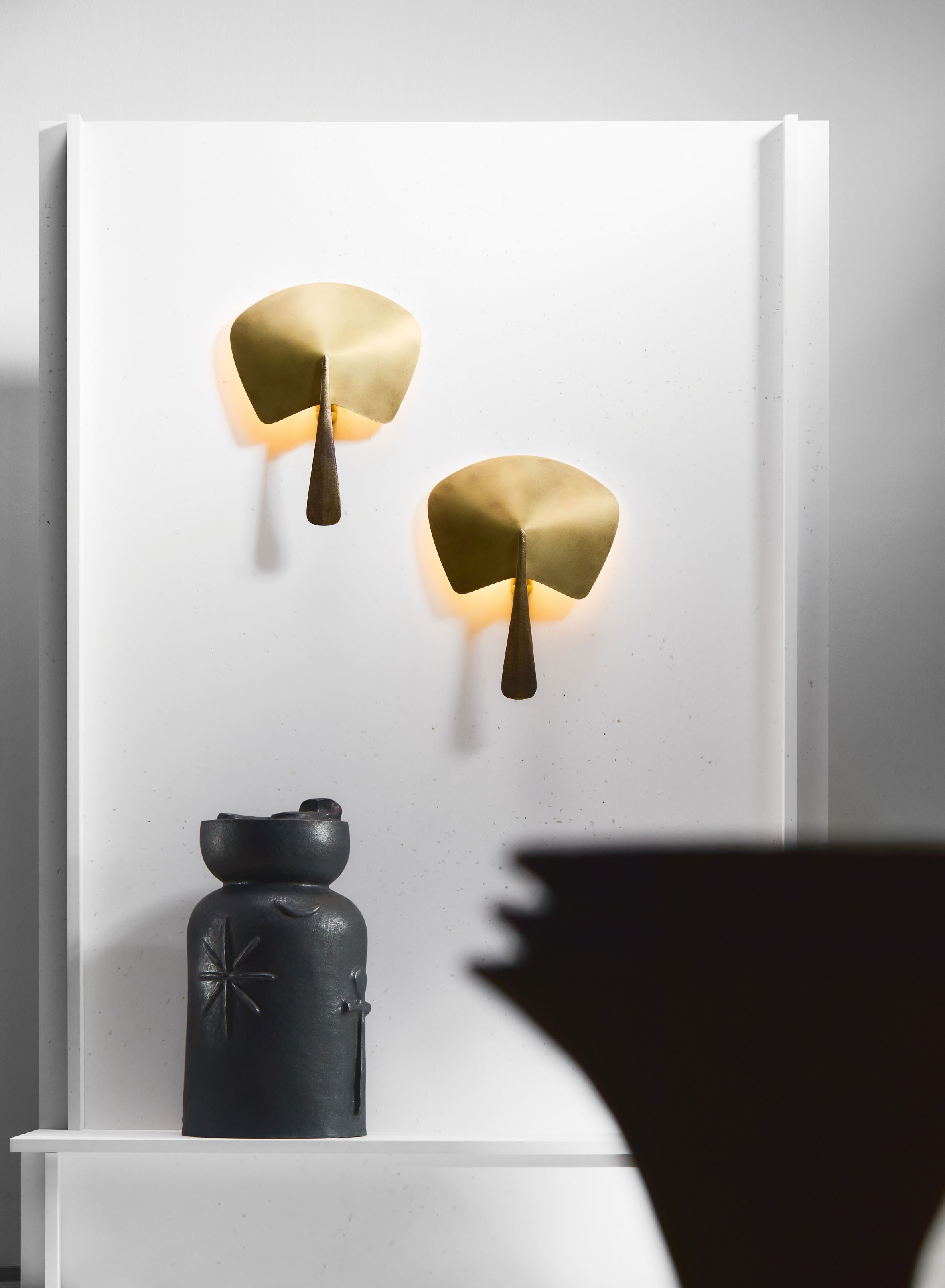 Two wall lamps made of cast bronze and aged brass, designed by Federico Stefanovich, displayed on a white wall alongside a dark ceramic vase.