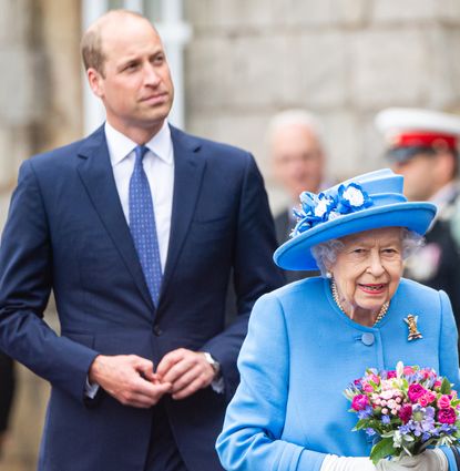 Prince William wearing a blue suit walking behind Queen Elizabeth, dressed in light blue