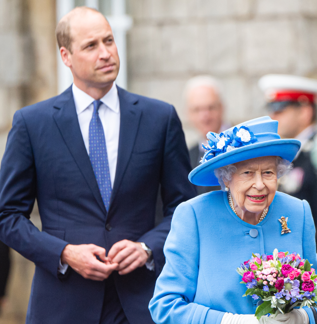 Prince William wearing a blue suit walking behind Queen Elizabeth, dressed in light blue