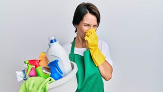 A woman holding her nose while carrying cleaning materials