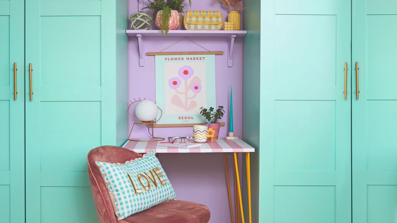 A small home office area with a striped desk with pin legs set between two turquoise wardrobes with panelled doors and brass handles