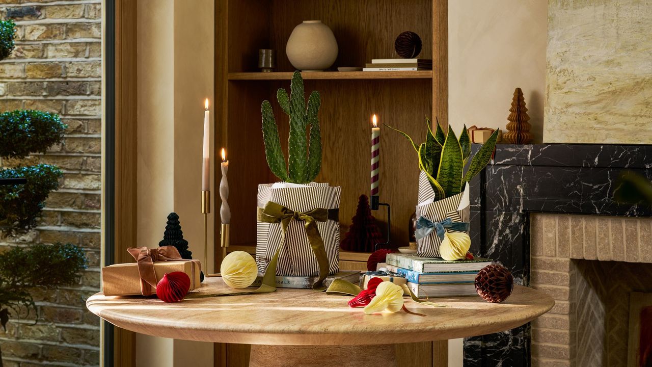 A marble table with a potted cactus and a potted snake plant surrounded by taper candles, paper ornaments, and ribbons