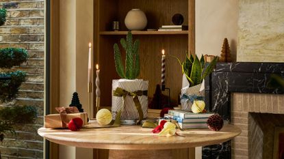 A marble table with a potted cactus and a potted snake plant surrounded by taper candles, paper ornaments, and ribbons