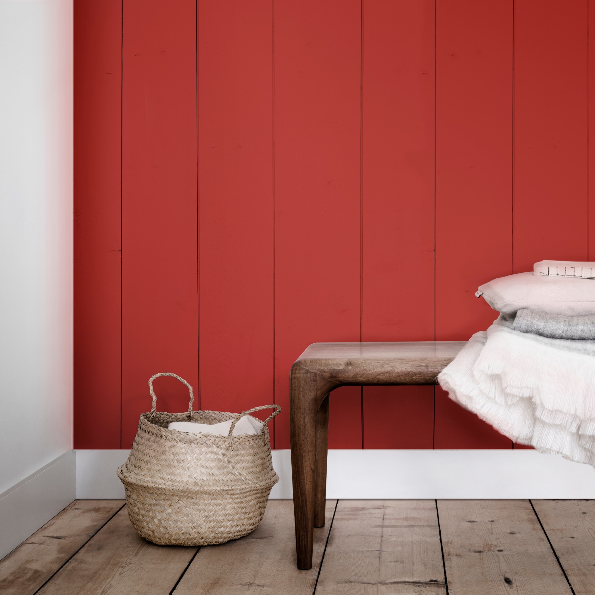 A hallway with wooden floors, a wooden bench and a panelled wall painted in red