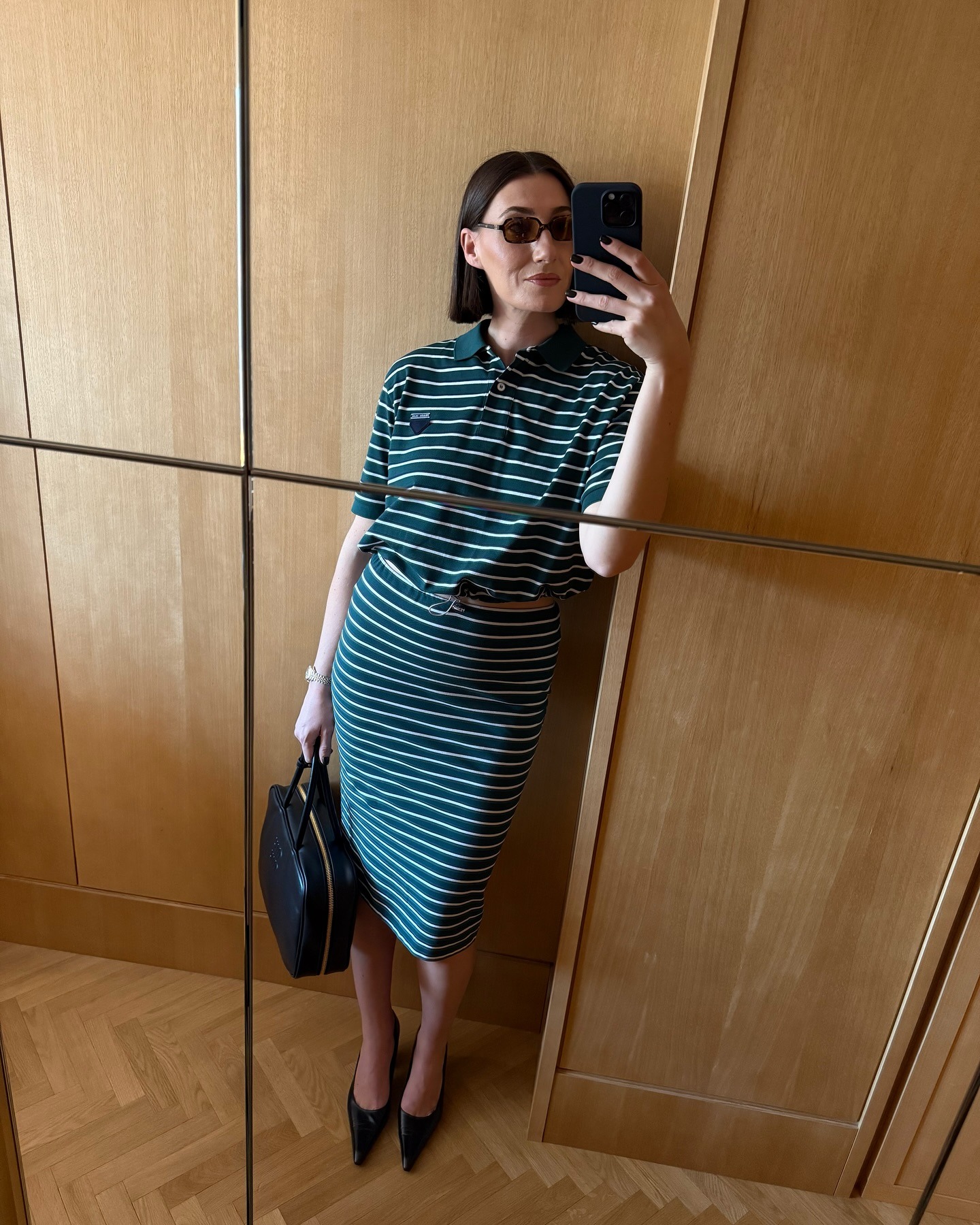 Woman wears green and white striped top and skirt and carries black Miu Miu bag