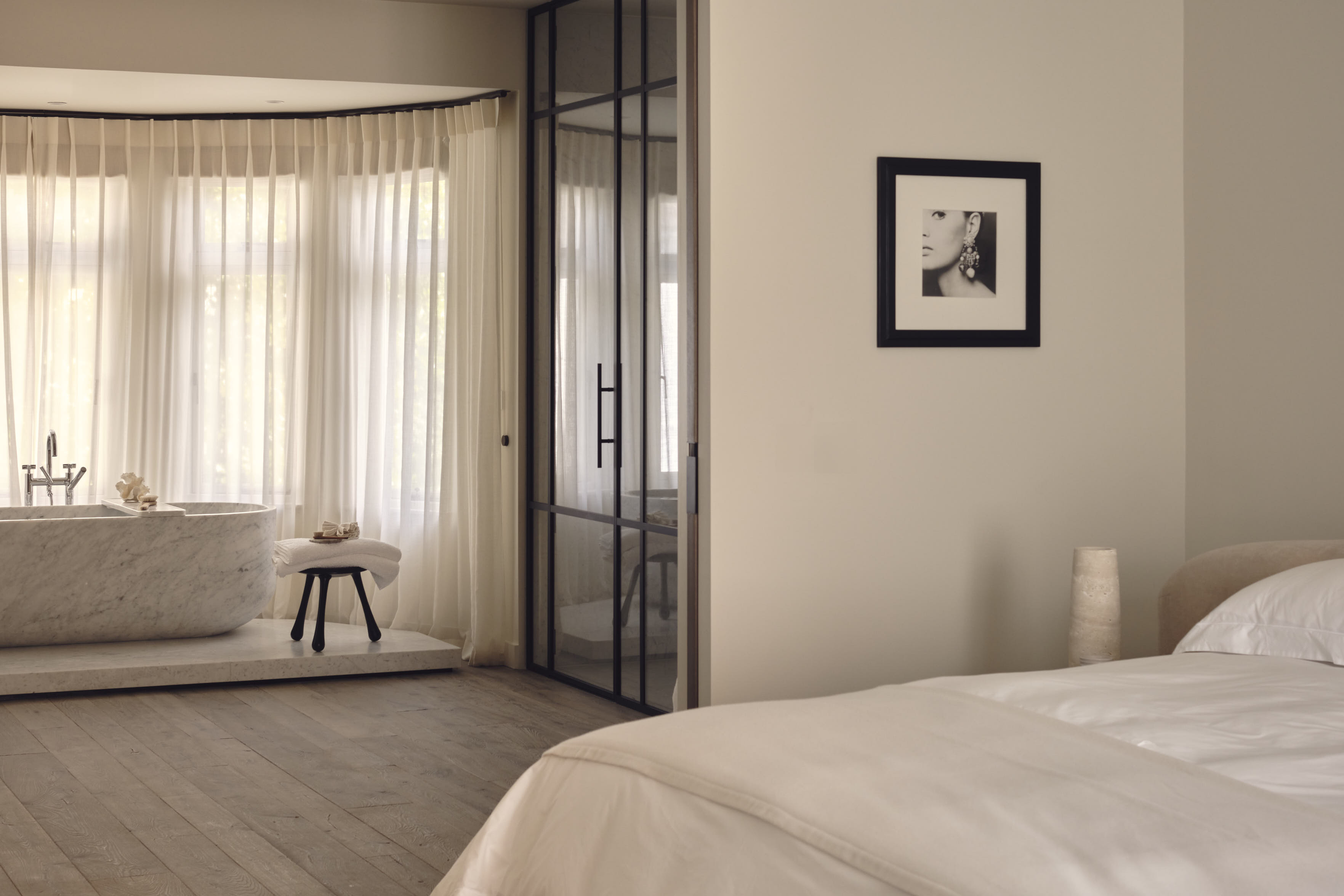 modern bedroom with marble bath on platform with sheer curtains around, enclosed shower, and bed mad with white sheets