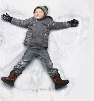A young boy making snow angels.