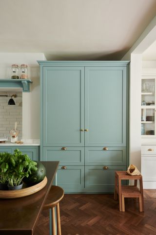 a mint green kitchen cabinet with gold handle accents in a wood and white themed kitchen, serving as a great pop of color