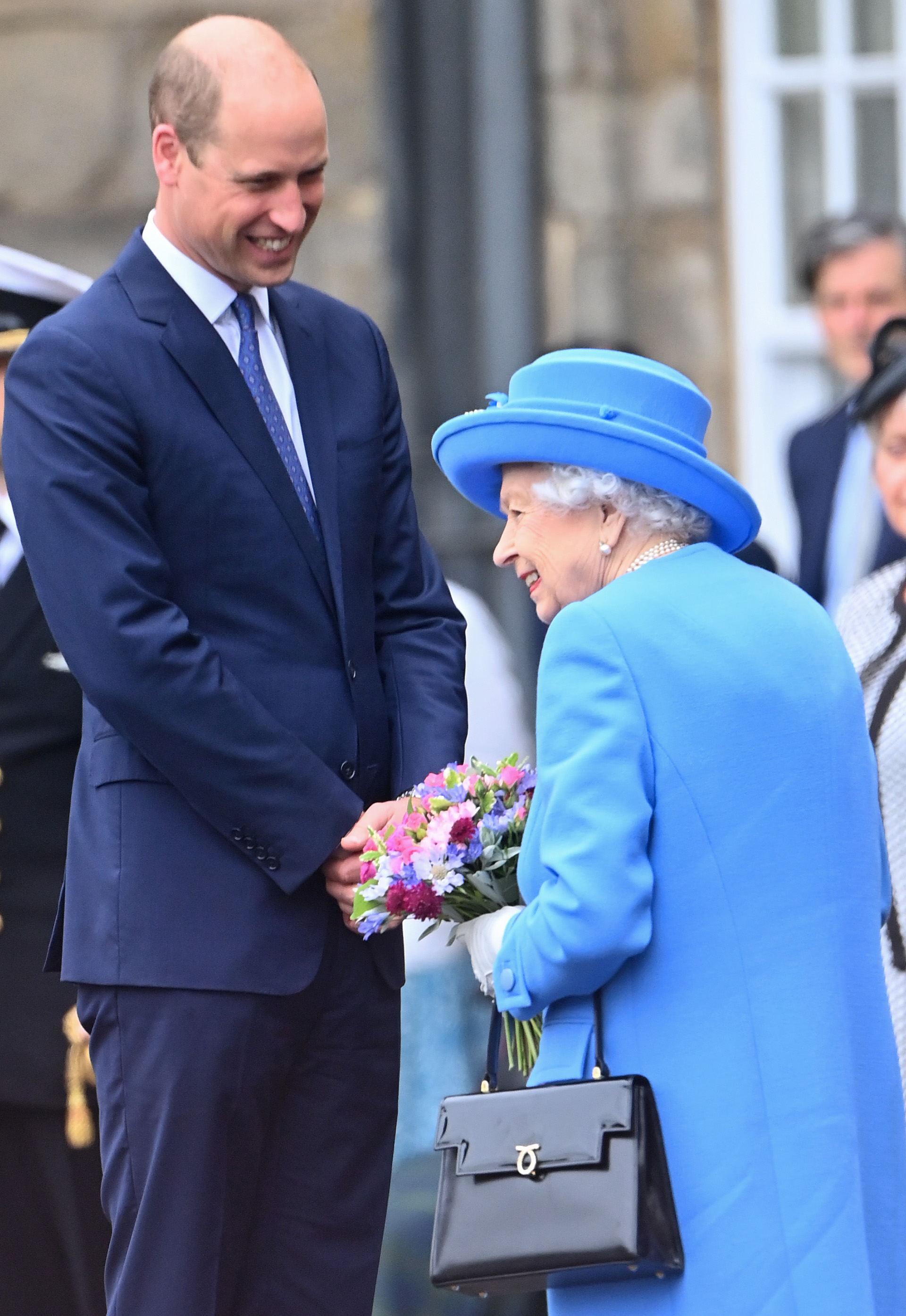 Queen Elizabeth in a blue coat laughing with Prince William