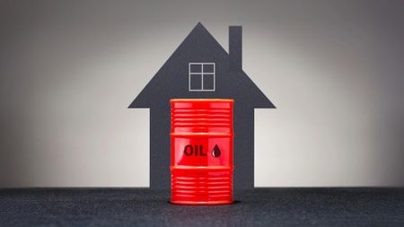 Graphic showing red barrel of oil in front of a grey background and the outline of a house. 