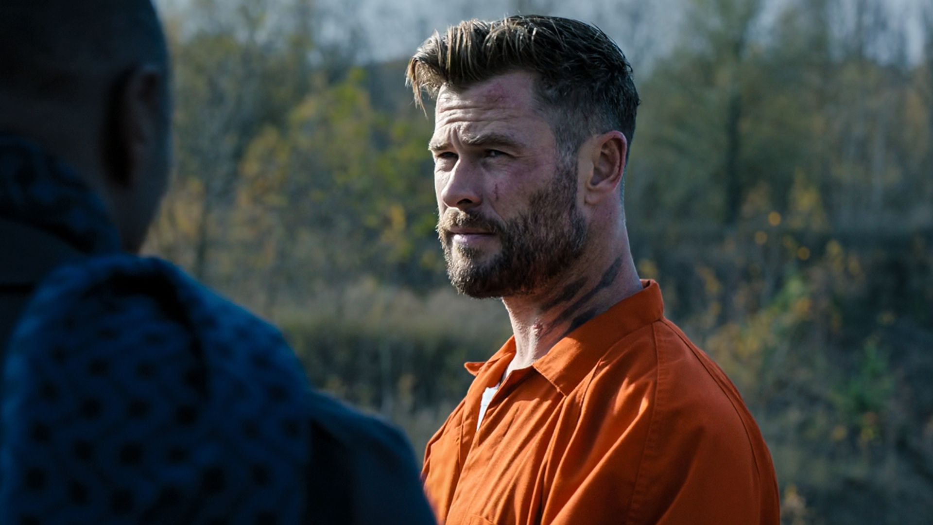 Chris Hemsworth wearing prison orange and neck tattoo in Extraction 2.