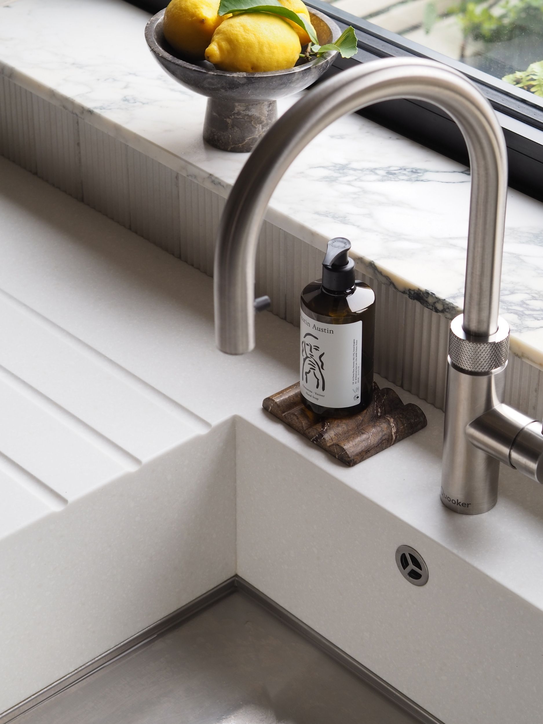 a kitchen sink ith a marble window sill behind, and a quooker tap