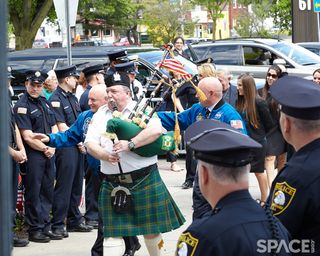 Bagpipe player precedes astronaut twins on a path lined by ceremonial police and firemen