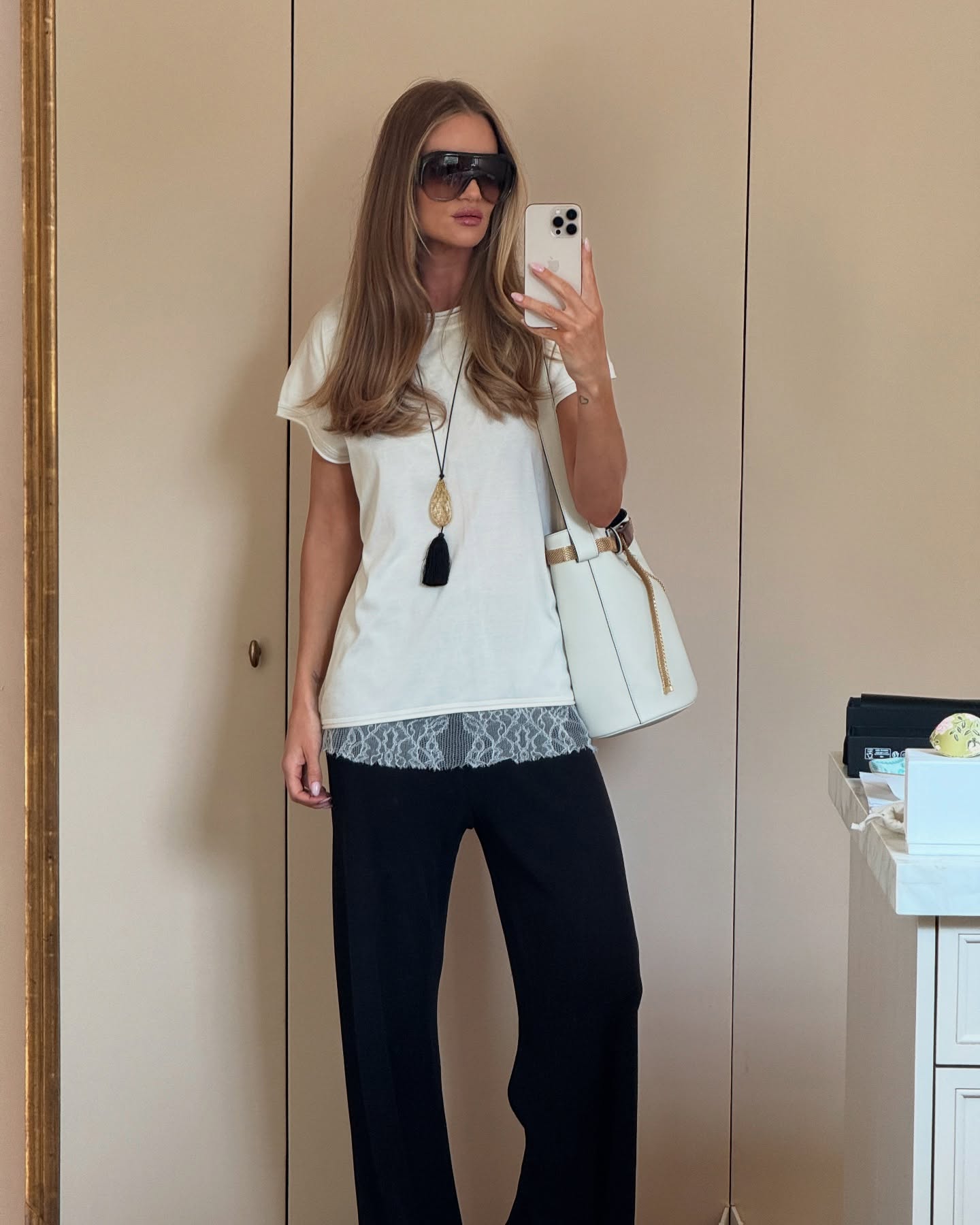 Rosie Huntingdon Whiteley wears a white top, black trousers and white Prada Buckle bag