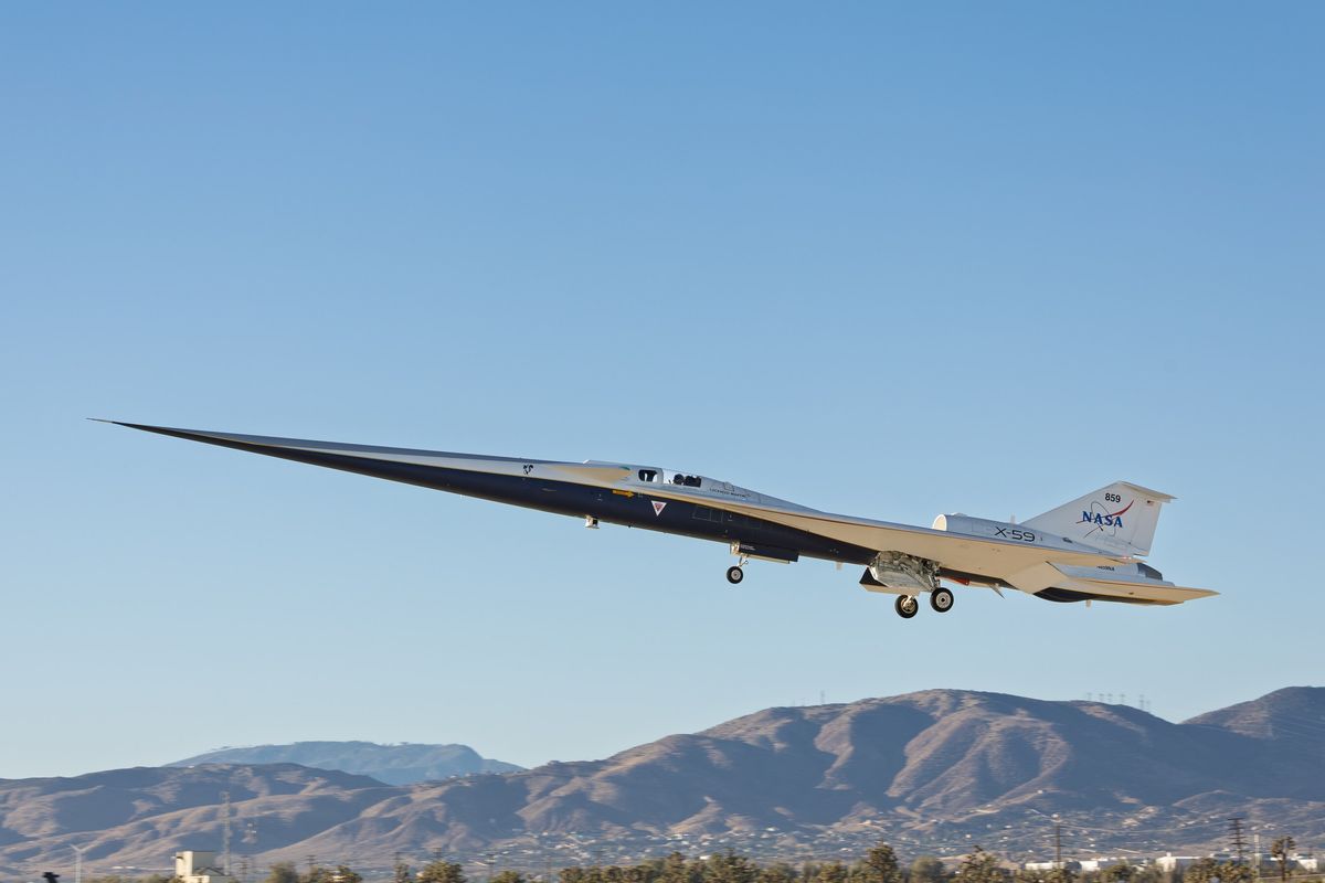 an elongated blue-and-white jet takes off under a cloudless blue sky
