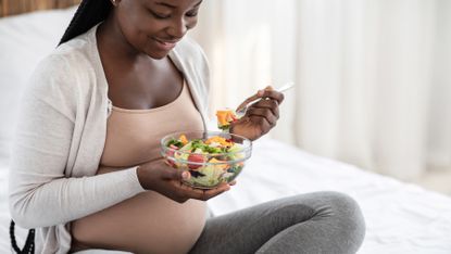 Happy pregnant woman eats a bowl of colorful salad