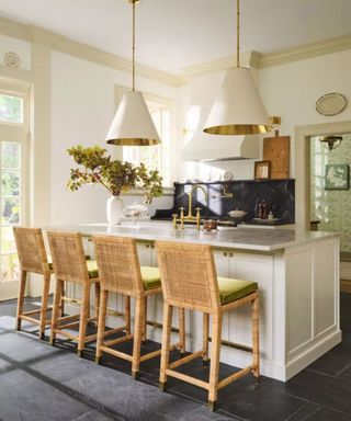 Four bar stools around a white kitchen island with brass faucet; two white pendant lights suspended from the ceiling.