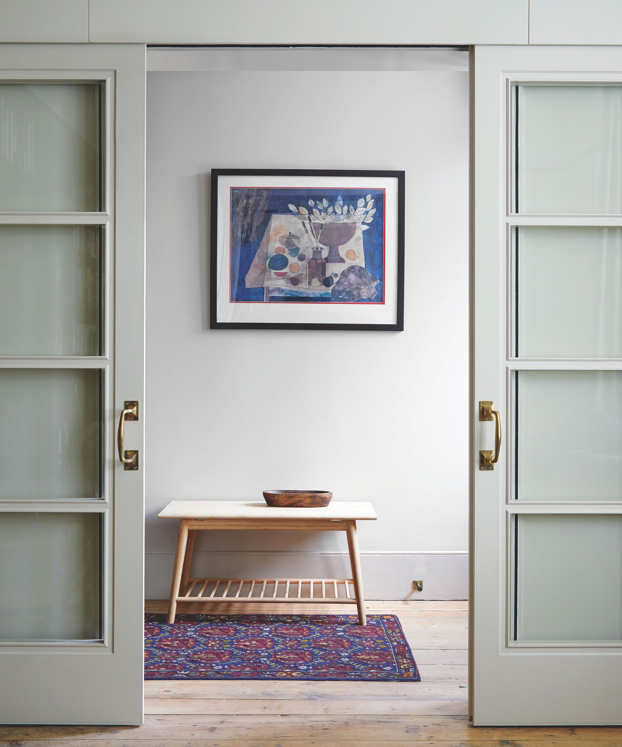two sliding glass-panel doors with gold hardware leading to a hallway with a rug on the floor, a small table, and artwork on the wall
