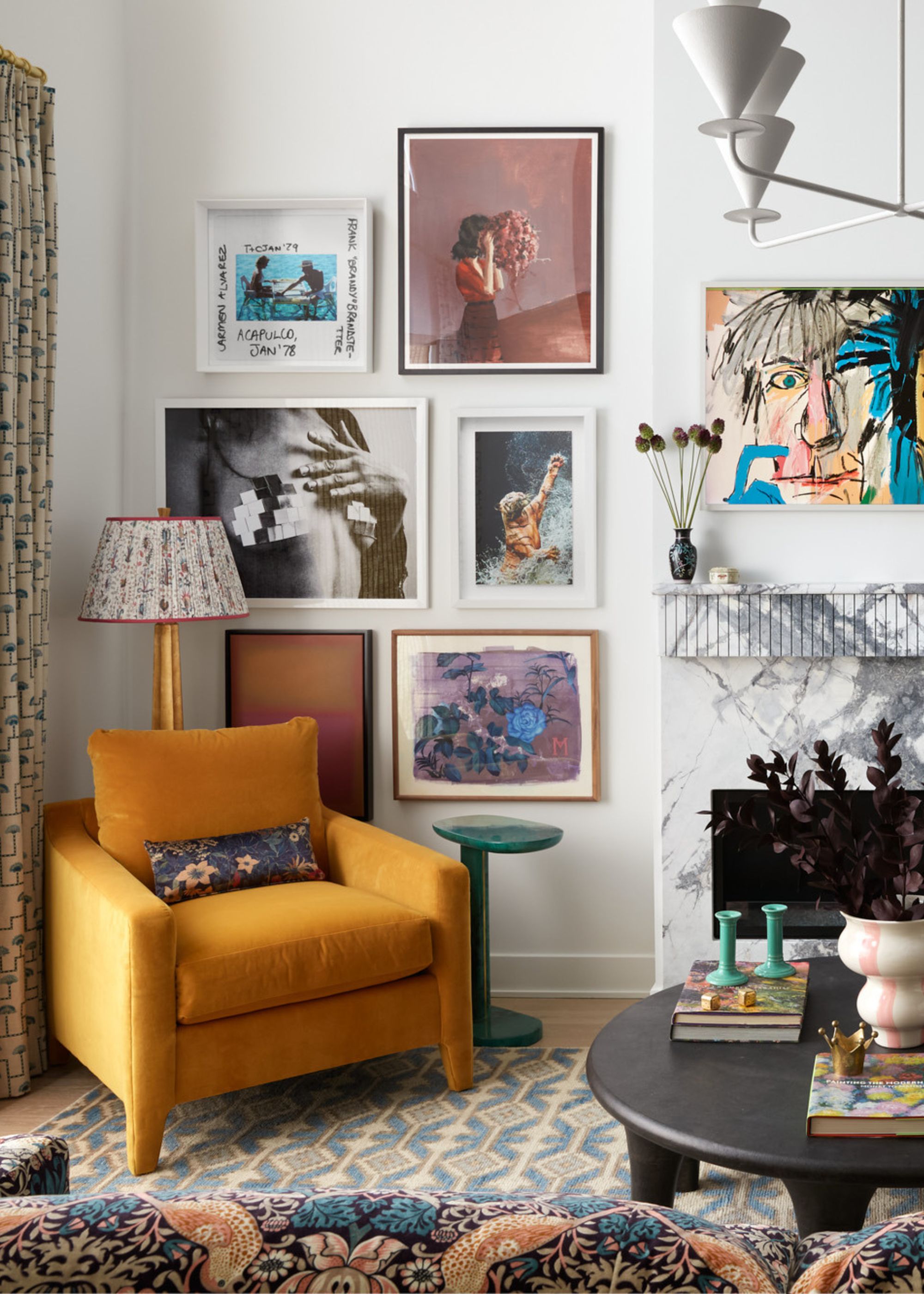 A maximalist living room with white walls, a gallery wall of artwork and photos, a marble fireplace, a mustard yellow armchair, and a blue patterned rug.