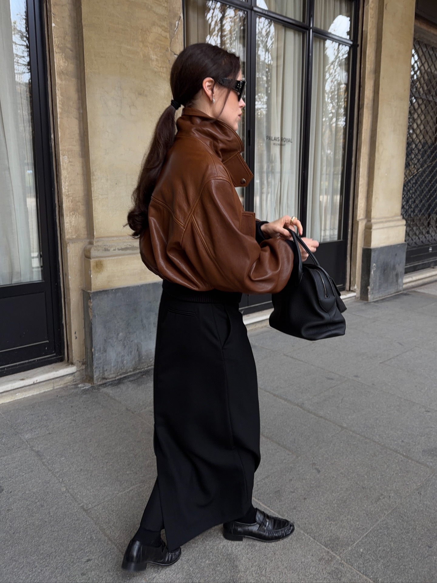 A woman walking wearing a brown oversized bomber jacket with a sleeky, shiny ponytail