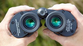 Close-up of a pair of black binoculars held between two hands.