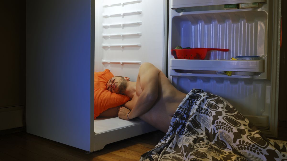 A man lies next to an open fridge door to stay cool when trying to sleep in hot weather