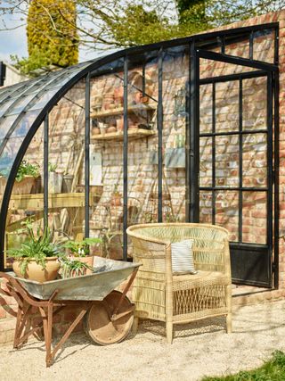 rustic garden set up with greenhouse, chair and wheelbarrow