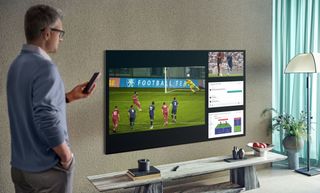 Sports playing on the Samsung QN95A as a man watches with remote