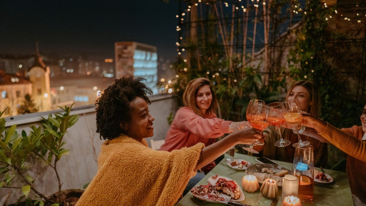 Friends gather for dinner at someone&#039;s balcony, and toast with wine. 