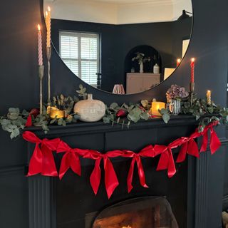 A black-painted fireplace against a matching black wall decorated with a red bow Christmas garland