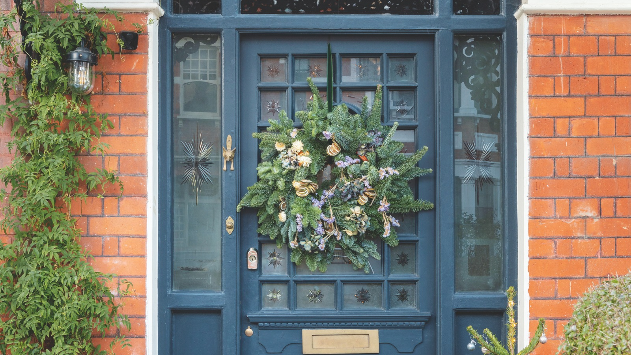 Wreath hanging on blue front door of a red brick house.