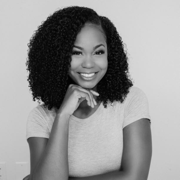 A black and white headshot featuring a woman with curly hair, Sabrina Porsche, smiling.
