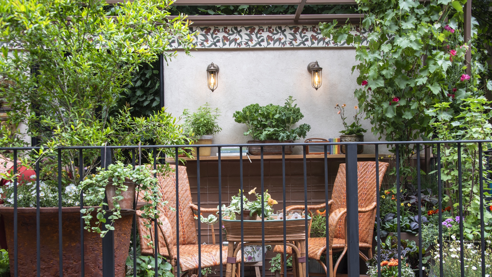Balcony garden with two vintage brown wicker chairs, surrounded by lots of pots