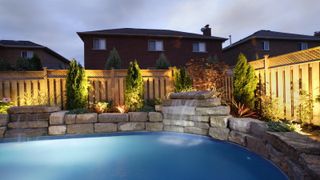 illuminated swimming pool surrounded by stones and well lit timber fencing