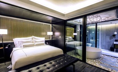 Bedroom featuring black wood flooring, black leather padded bench and en-suite bathroom