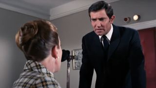 George Lazenby stands tensely at Moneypenny's desk in On Her Majesty's Secret Service.