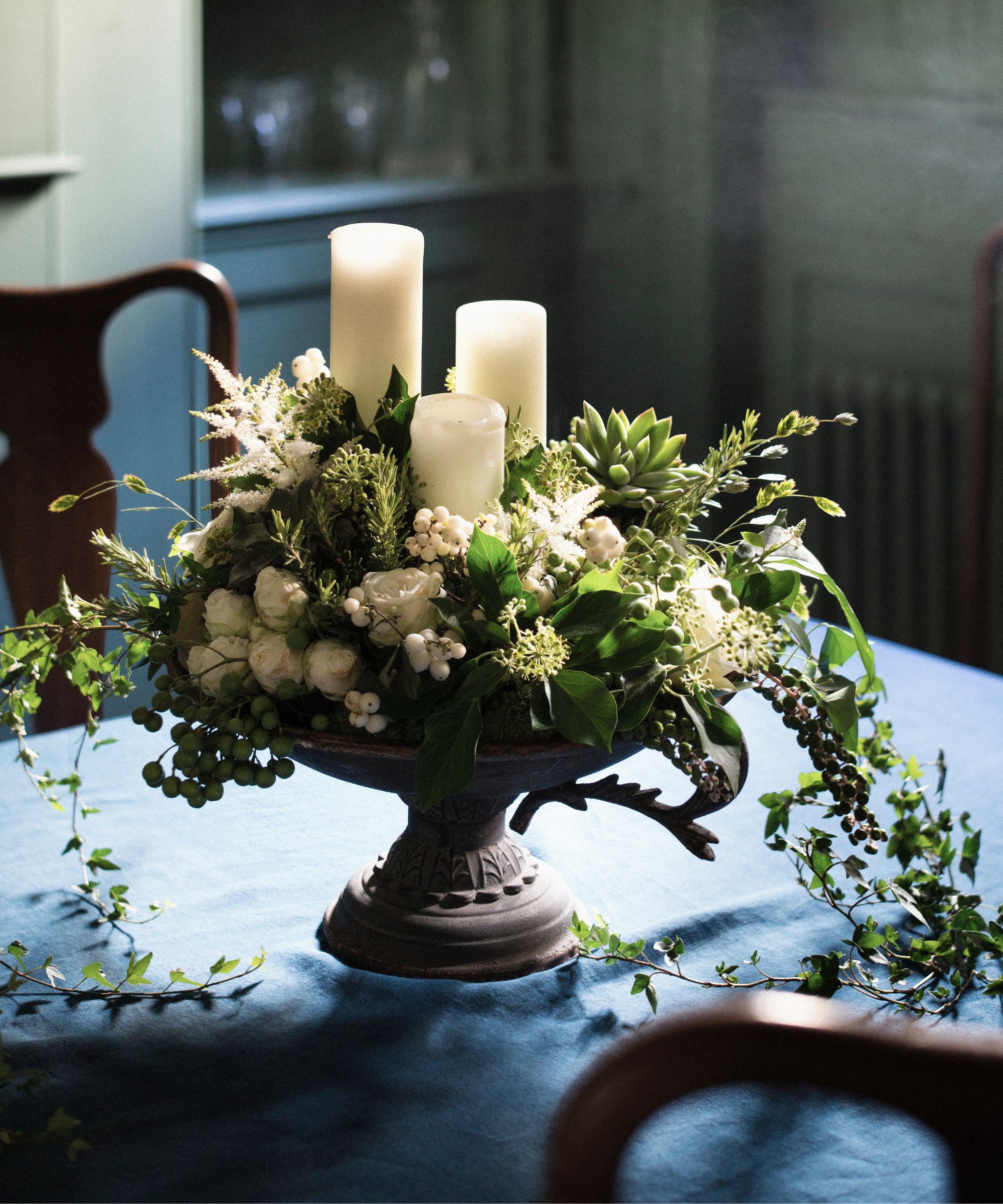 Footed stone bowl containing white floral arrangement and white pillar candles
