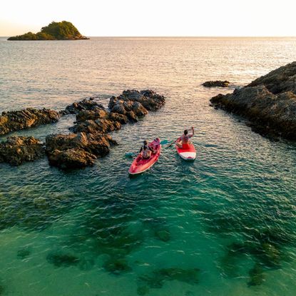 Two people in kayaks on a blue ocean, at sunset.