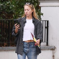 Lila Moss steps outside wearing mid-rise bootcut jeans with black ballet flats, a white tee and a flannel shirt.